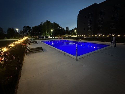 A swimming pool lit up at night with lights around it.
