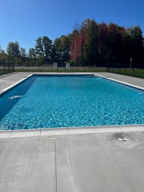 A large swimming pool with a grey deck and trees in the background.