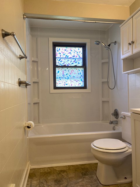 A white toilet sits in a bathroom with a stained glass window above it.
