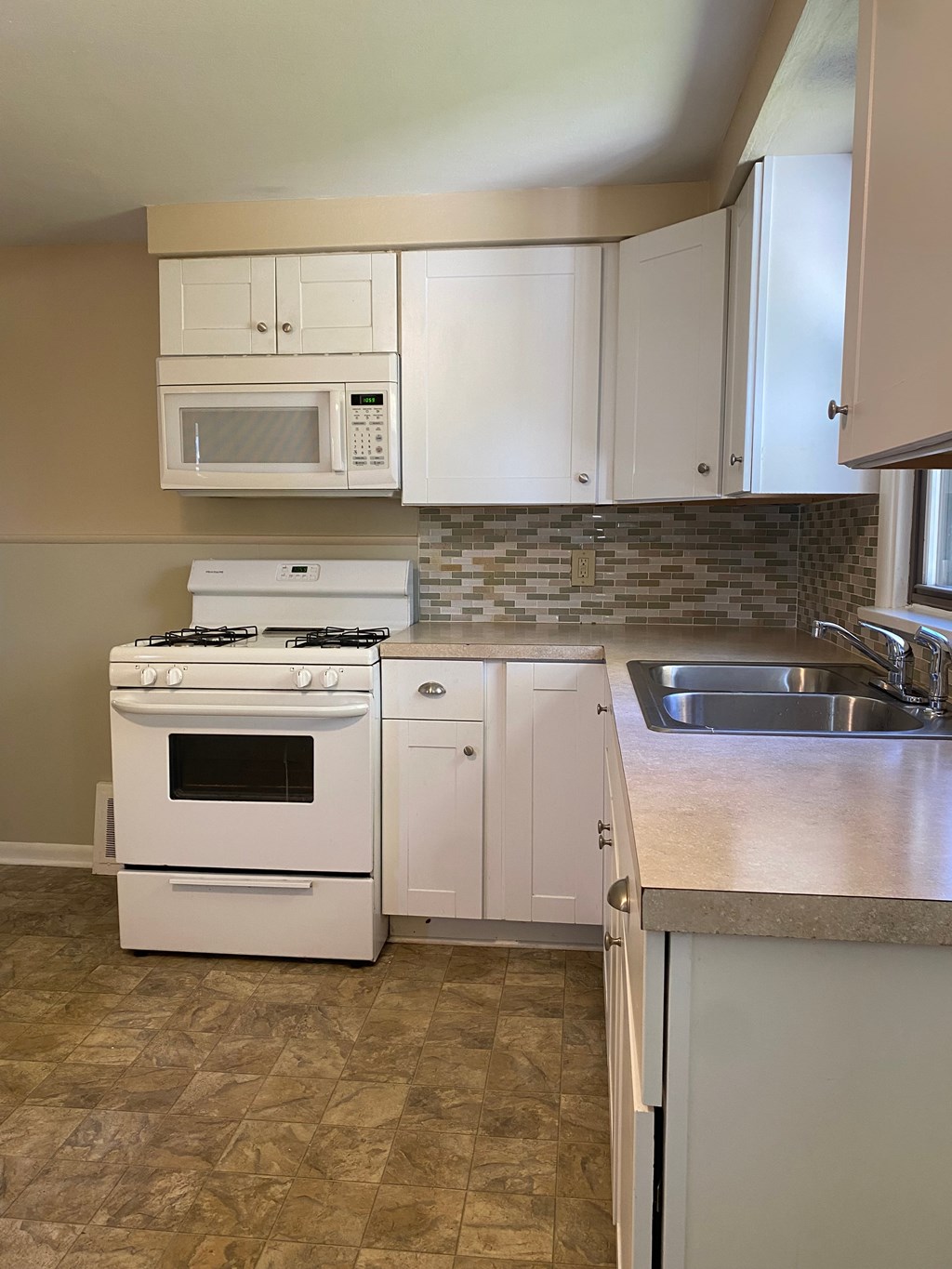 A kitchen with a white stove, white cabinets, and a white microwave.