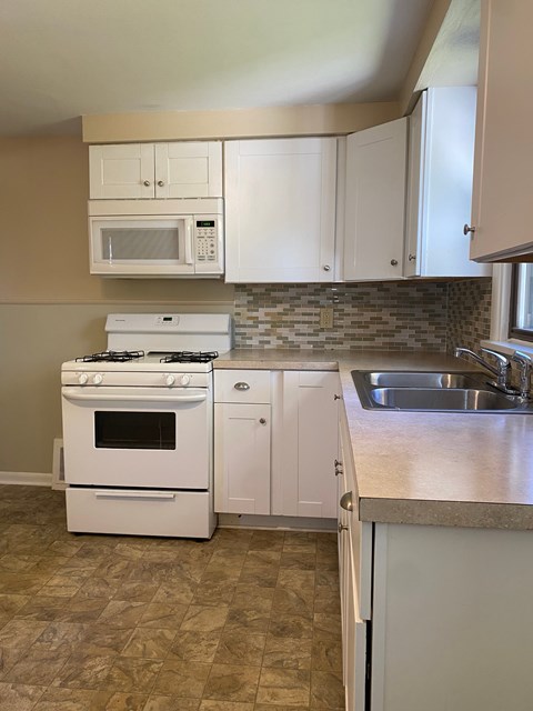 A kitchen with a white stove, white cabinets, and a white microwave.