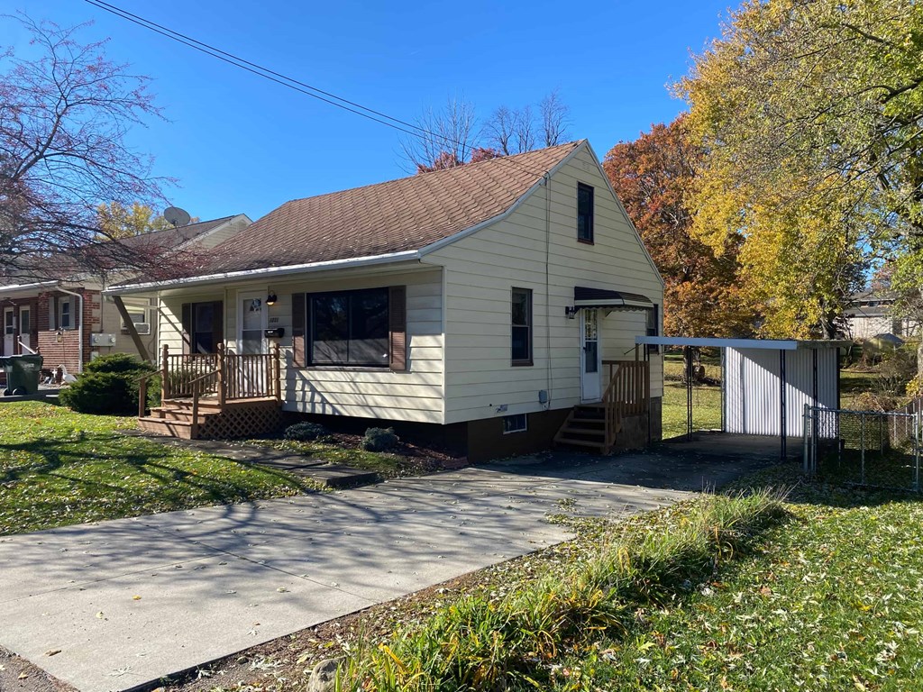 A house with a brown roof and a white exterior is surrounded by trees with autumn foliage.