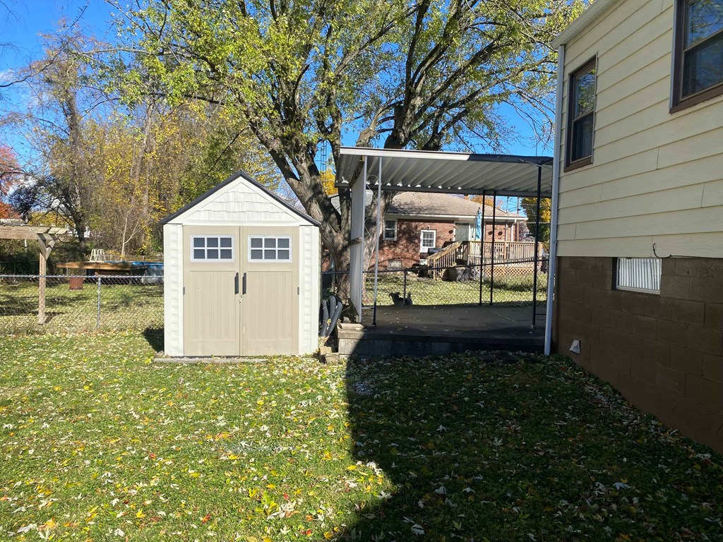 A small white shed sits in a grassy area next to a house.