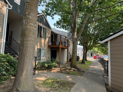 A tree in front of a building with a black railing.