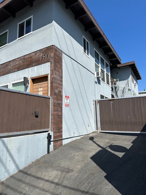 A grey building with a brown door and a red and white sign on the wall.