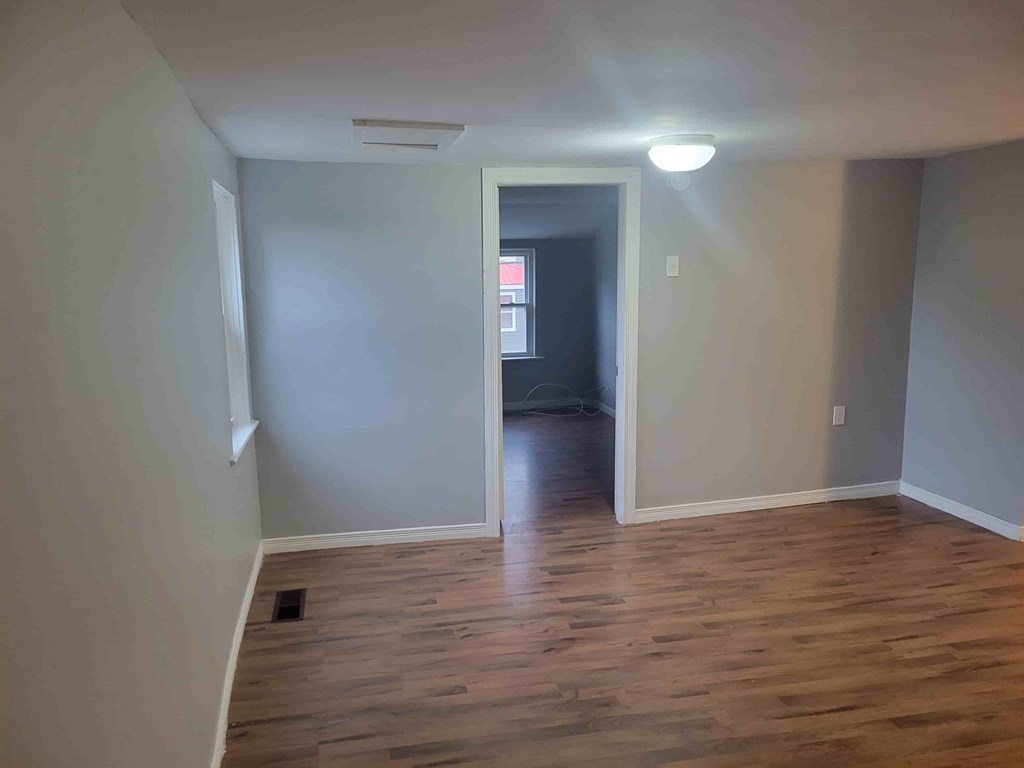 A room with wooden flooring and a doorway leading to another room.