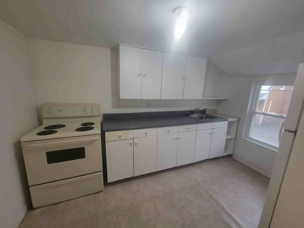 A kitchen with a stove, sink, and cabinets.
