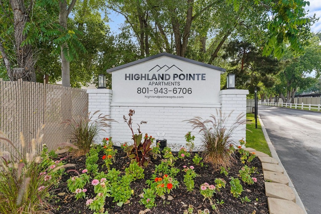 A sign for Highland Pointe Apartments is surrounded by flowers and greenery.