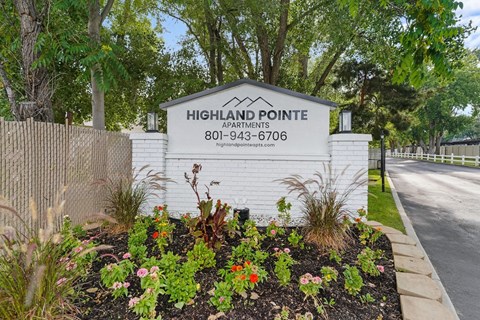 A sign for Highland Pointe Apartments is surrounded by flowers and greenery.