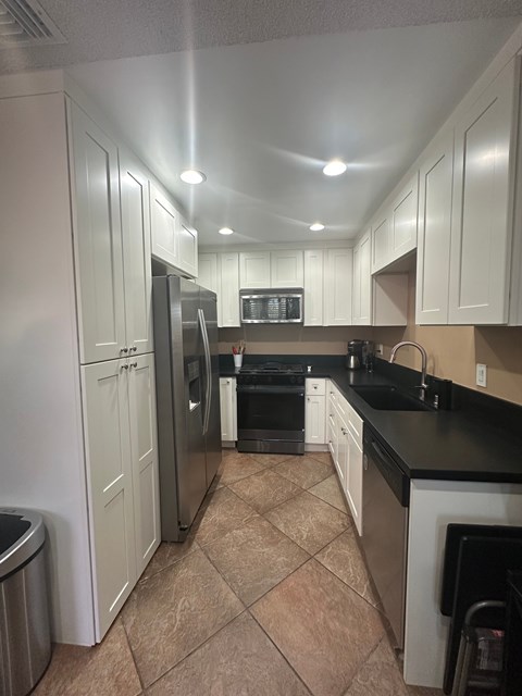 A kitchen with white cabinets and black countertops.