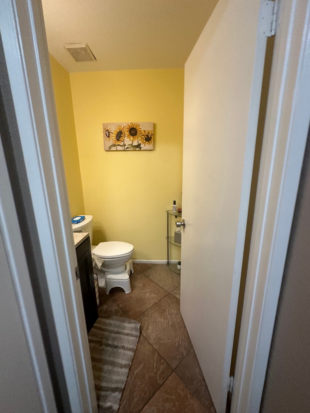 A bathroom with a toilet, sink, and a painting on the wall.