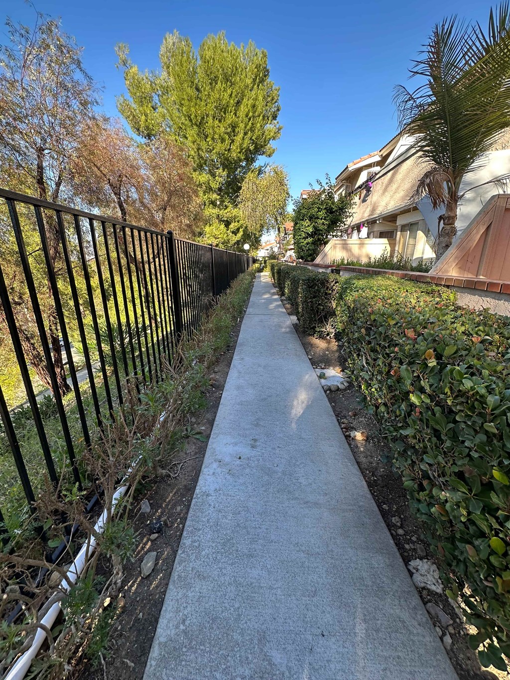 A sidewalk runs down a hillside with a metal fence on the left and a building on the right.
