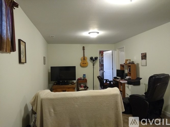 A room with a bed, a desk, a chair, a guitar, and a television.