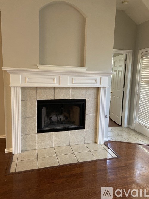 A white fireplace with a black grate in a room with wooden floors.