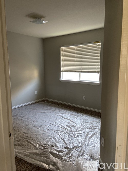 A room with a bed covered in plastic and a window with blinds.