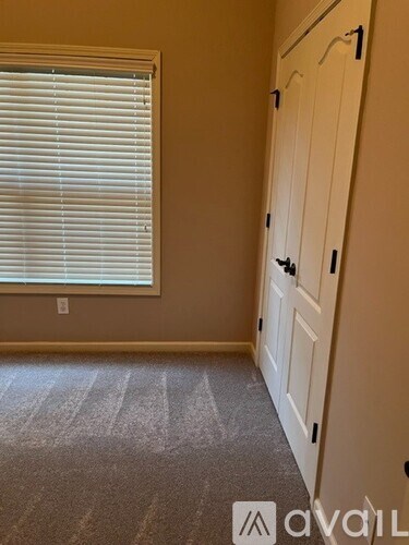 A room with a carpeted floor, a window with blinds, and a door with a handle.