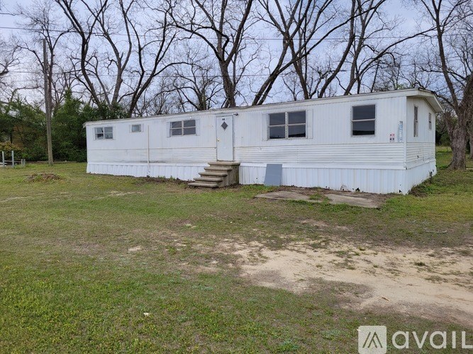 A white mobile home sits in a grassy field with trees in the background.