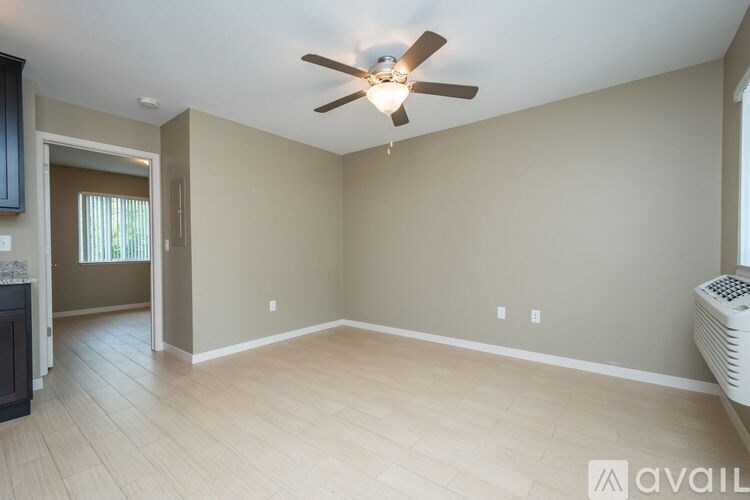 A spacious room with a ceiling fan and light, hardwood floors, and a window with blinds.