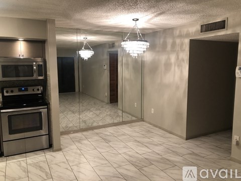 A kitchen with a stove top oven and microwave, a tiled floor, and a chandelier hanging from the ceiling.