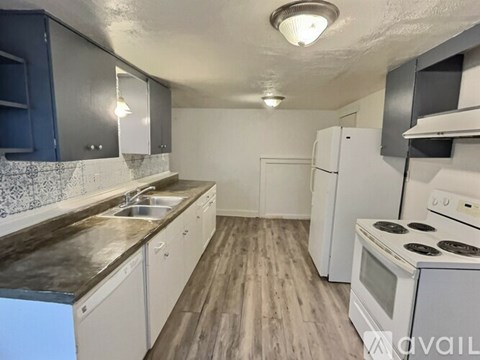 A kitchen with white appliances and a wooden floor.
