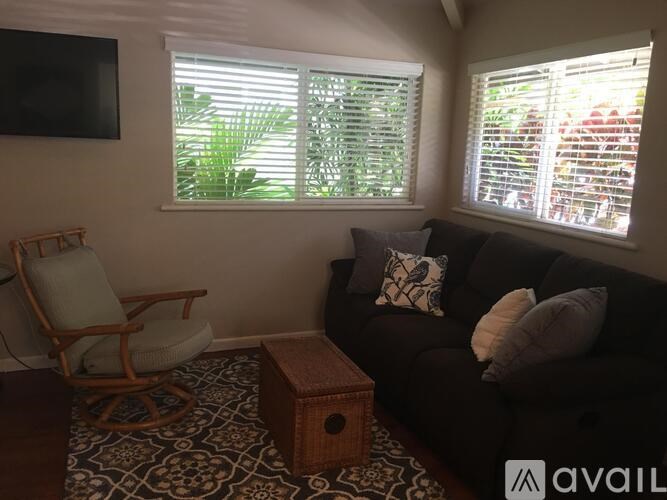 A living room with a black couch, a wooden chair, and a TV mounted on the wall.