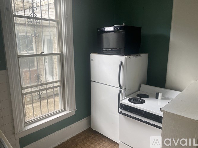 A white refrigerator with a black box on top sits in a kitchen next to a window.