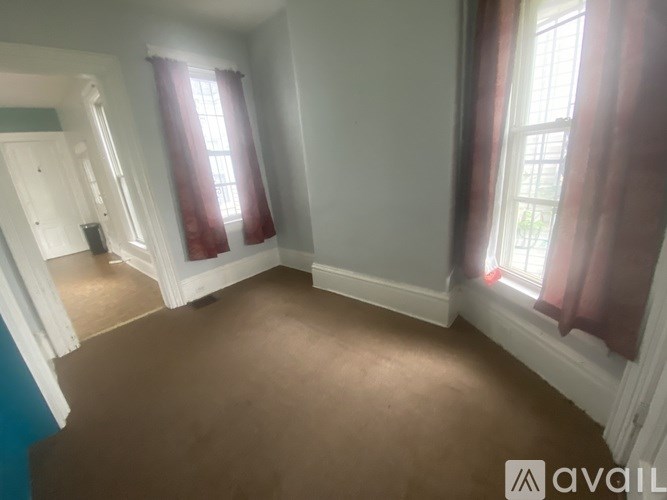 A room with brown carpet and two windows with red curtains.