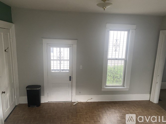 A room with a white door, a window, and a trash can.