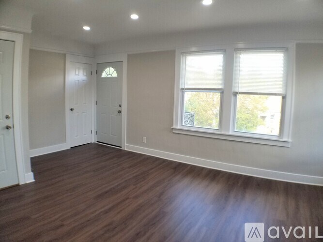 A room with wooden floors and white walls, with a window on the right side.
