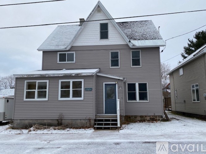 A house with a grey siding and a white roof with snow on the ground.