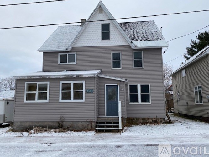 A house with a grey siding and a white roof with snow on the ground.