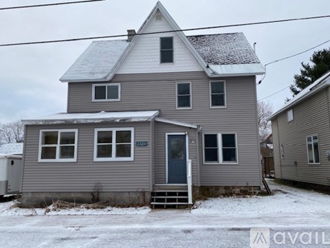 A house with a grey siding and a white roof with snow on the ground.