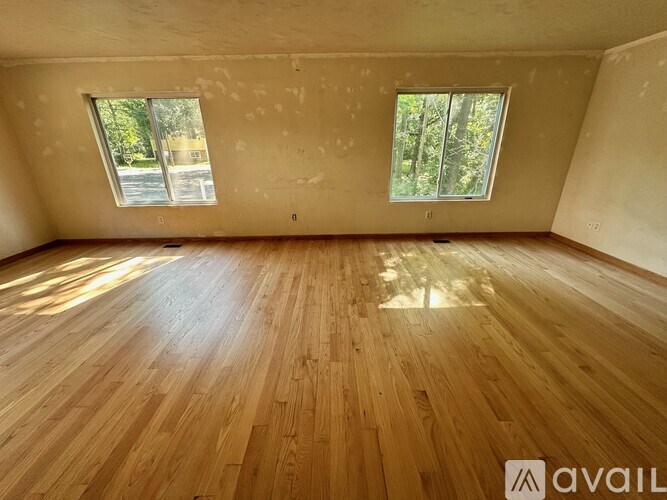 A room with wooden flooring and two windows.