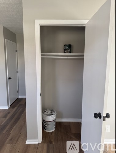 A white door is open to a small pantry with a shelf and a bucket of paint on the floor.