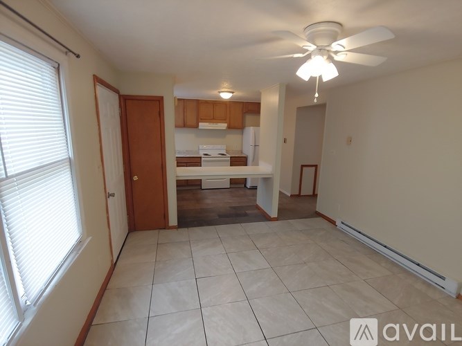 A living room with a fan and a kitchen in the background.
