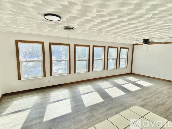 A room with a white ceiling, wooden floor, and a window with a view of trees outside.