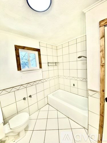 A bathroom with a toilet, a tub, and a window.