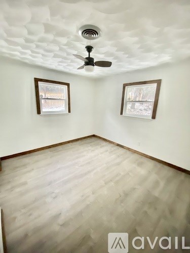 A room with a ceiling fan and two windows.