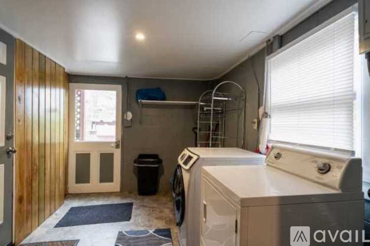 A laundry room with a washer and dryer, a window with blinds, and a door leading outside.