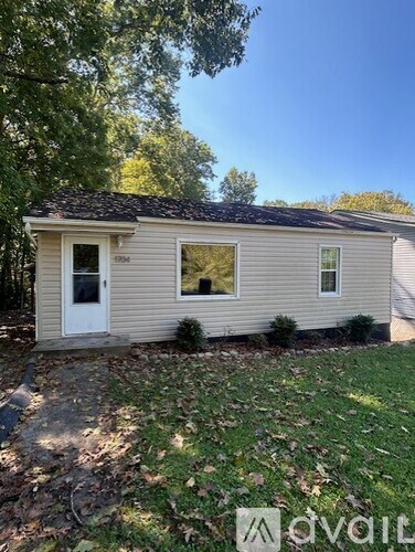A small house with a white door and windows is surrounded by trees.