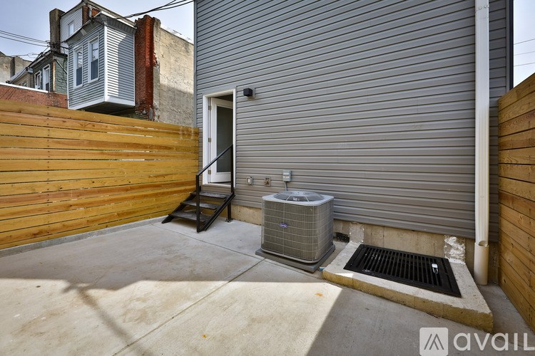 A small outdoor patio with a concrete floor, a wooden fence, and a metal air conditioning unit.