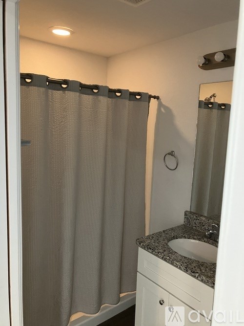 A bathroom with a shower curtain, sink, and mirror.