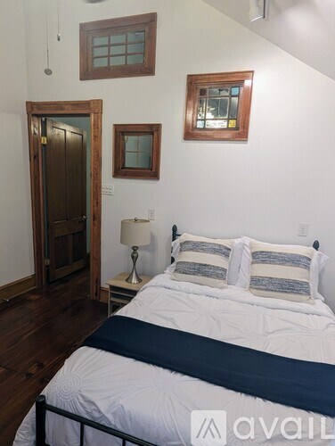 A bedroom with a bed, lamp, and two windows.