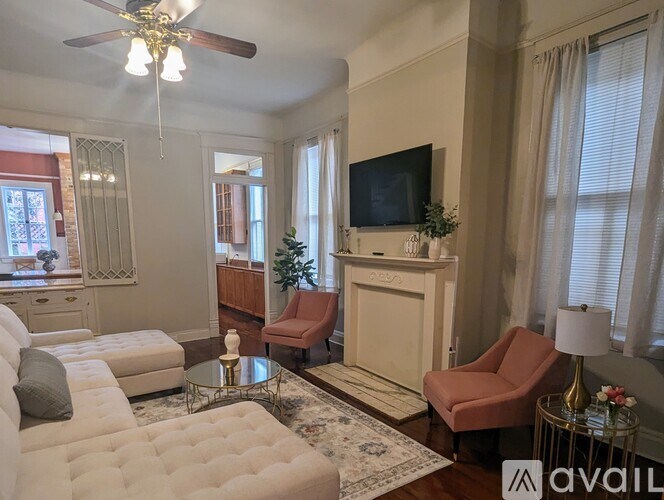 A living room with a white couch, a red chair, and a television mounted on the wall.