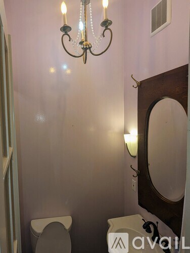 A bathroom with a toilet, mirror, and chandelier.