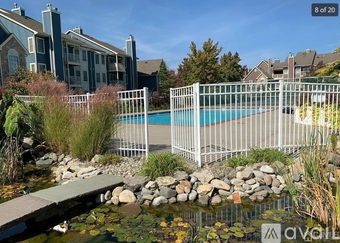 A pool surrounded by a white fence and a small bridge over a pond.