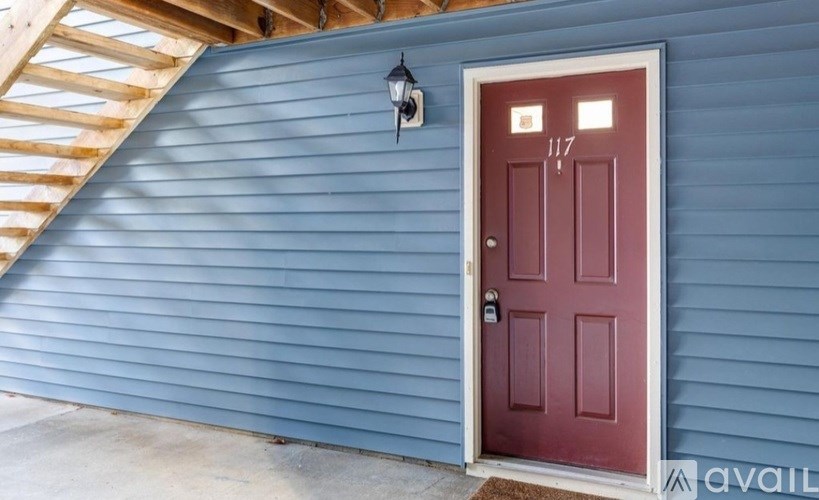 A red door with the number 117 on it is on a blue house.