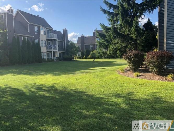A grassy area in front of a building with trees and bushes.