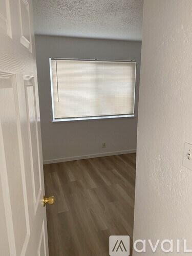 A hallway with a wooden floor and a window with blinds.