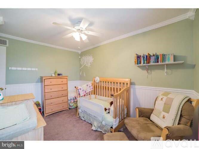 A baby room with a crib, a dresser, a chair and a ceiling fan.
